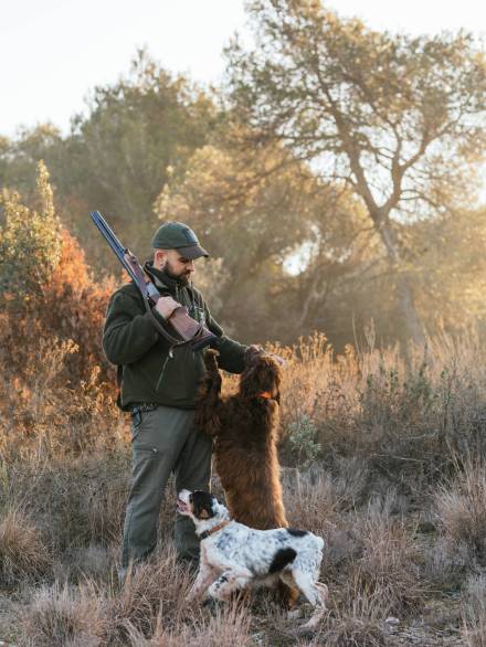 Hunter man holding a shotgun while hunting with his dogs outdoors in the field. Hunter man holding a shotgun while hunting with his dogs outdoors in the field. Hunting season concept.