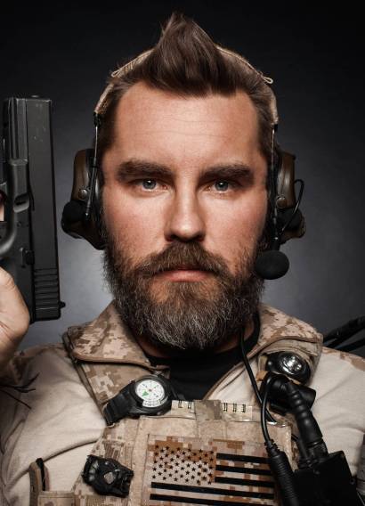 portrait of brutal man in military uniform. Close-up portrait of brutal bearded man in military desert uniform and body armor who holds his gun on black background. Studio photography of a player in airsoft.
